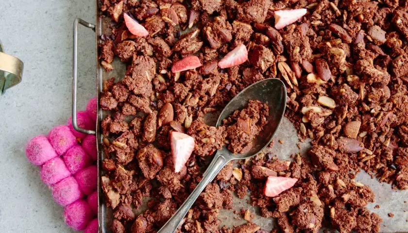 En sked tar en rejäl bit av hemgjord granola choklad med mandlar och jordgubbar.