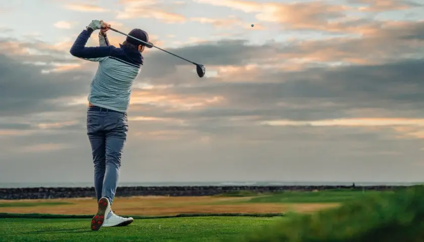 En golfare svingar klubban vid solnedgången. Ett perfekt sätt att använda sitt friskvårdsbidrag för golf.