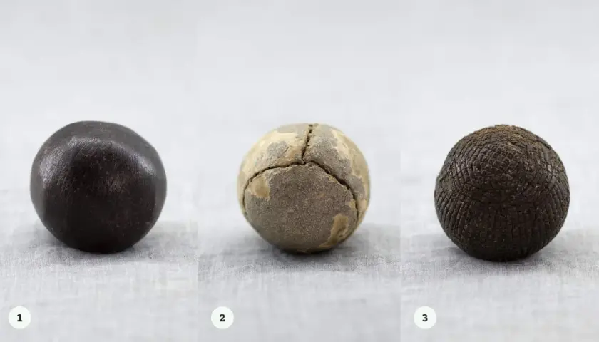Tre gamla bollar: en mörk, en sprickig och en med rutmönster. Kanske en tidig guttaperka boll?