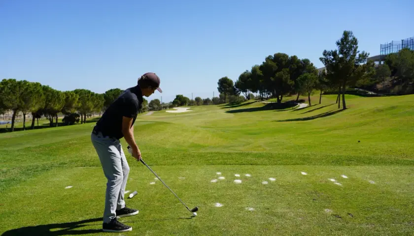 En man förbereder sig för ett slag på en golfbana. Han är klädd i en keps och tröja, redo för olika spelformer golf.