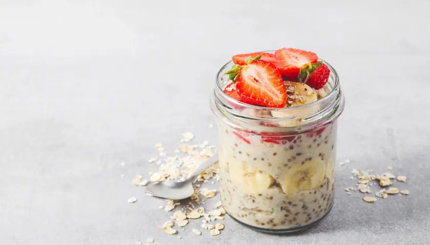 En burk med overnight oats recept toppad med jordgubbar och banan. En sked ligger bredvid med havregryn.