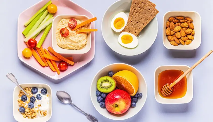 En frukost med kolhydratrik mat: yoghurt med granola och blåbär, frukt, ägg, kex, nötter, honung och grönsaksstavar med hummus.