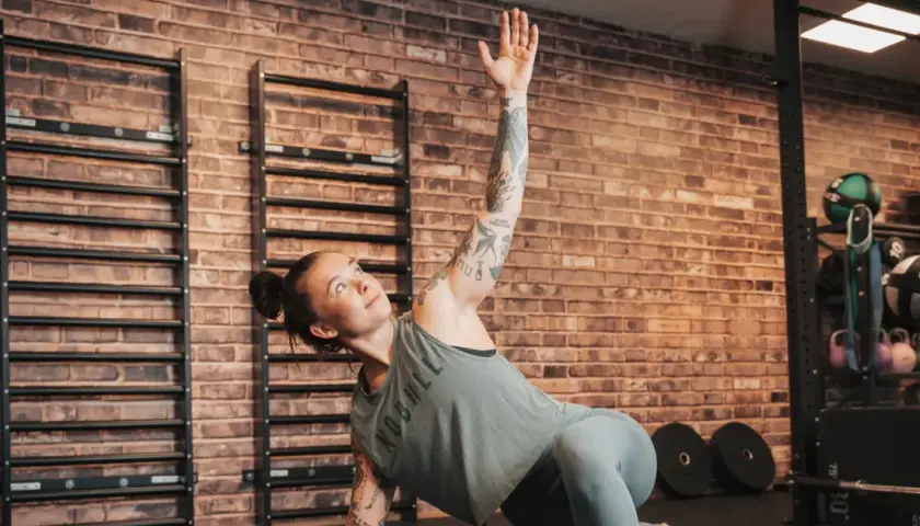Kvinna med tatueringar utför en övning på sitt gymprogram. Hon ligger på sidan med en arm uppsträckt.
