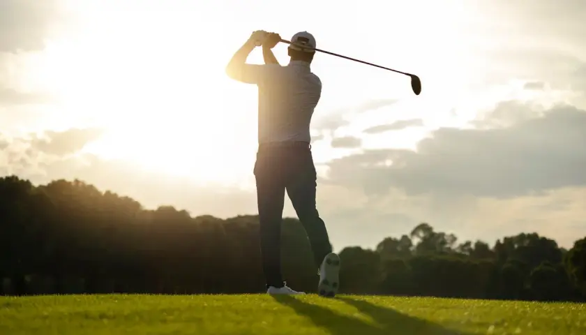 En golfare svingar klubban i solnedgången. Perfekt för en golf flyer.