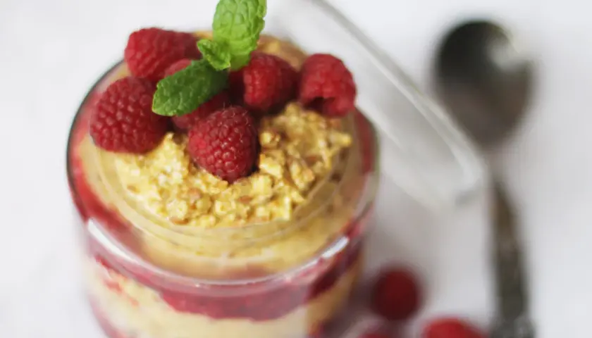 En burk med overnight oats med saffranssmak, toppad med hallon och mynta. En sked ligger bredvid.