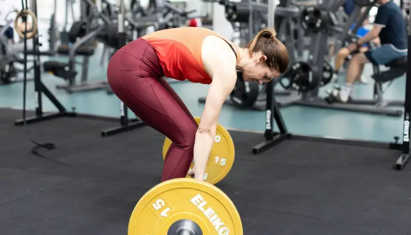 Kvinna förbereder sig för marklyft med en skivstång i ett gym. Hon böjer sig ner mot vikterna, redo att lyfta.