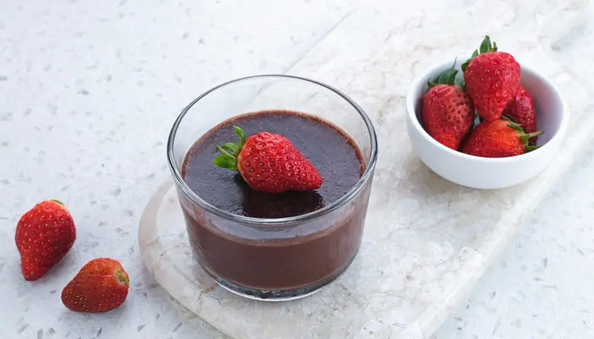 Chokladig proteinpudding i glas, toppad med jordgubbe. Bredvid en skål med färska jordgubbar. Ett enkelt recept på proteinpudding.
