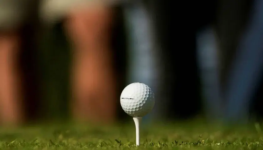 En golfboll i huvudet, redo för ett slag. Gräset är grönt och bakgrunden suddig.
