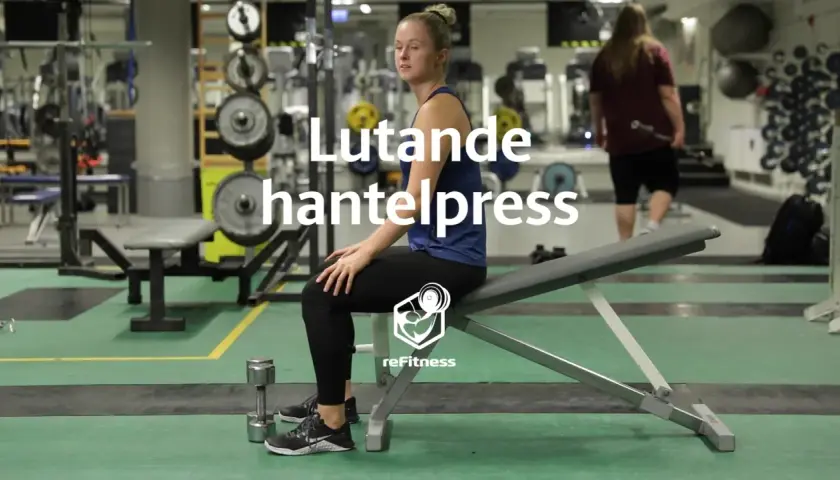 Kvinna förbereder sig för lutande hantelpress på gym. Hantlar ligger på golvet.