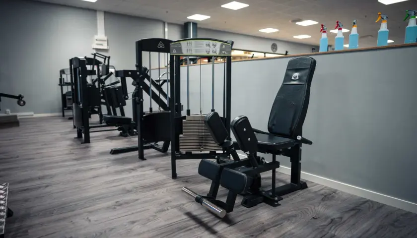 En adduktormaskin i ett modernt gym. Maskinen är svart med vadderade dynor och en viktstapel.