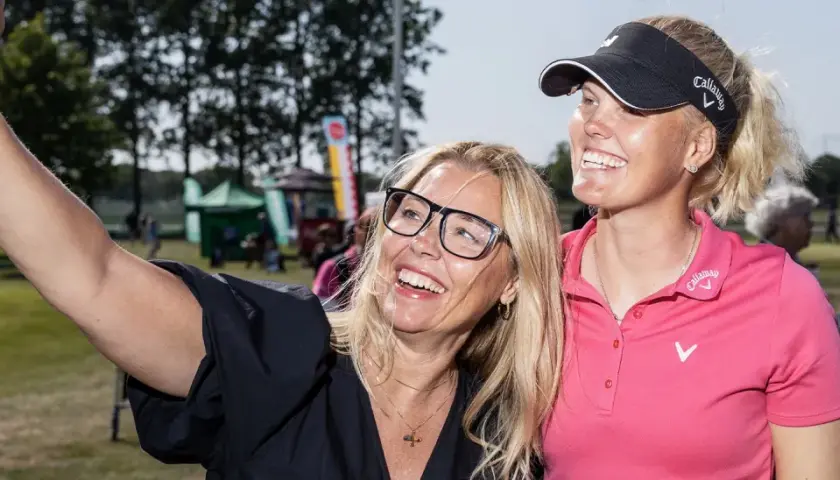 Två glada kvinnor tar en selfie vid Helsingborg Open. En kvinna med glasögon och en golfare i rosa tröja ler mot kameran.