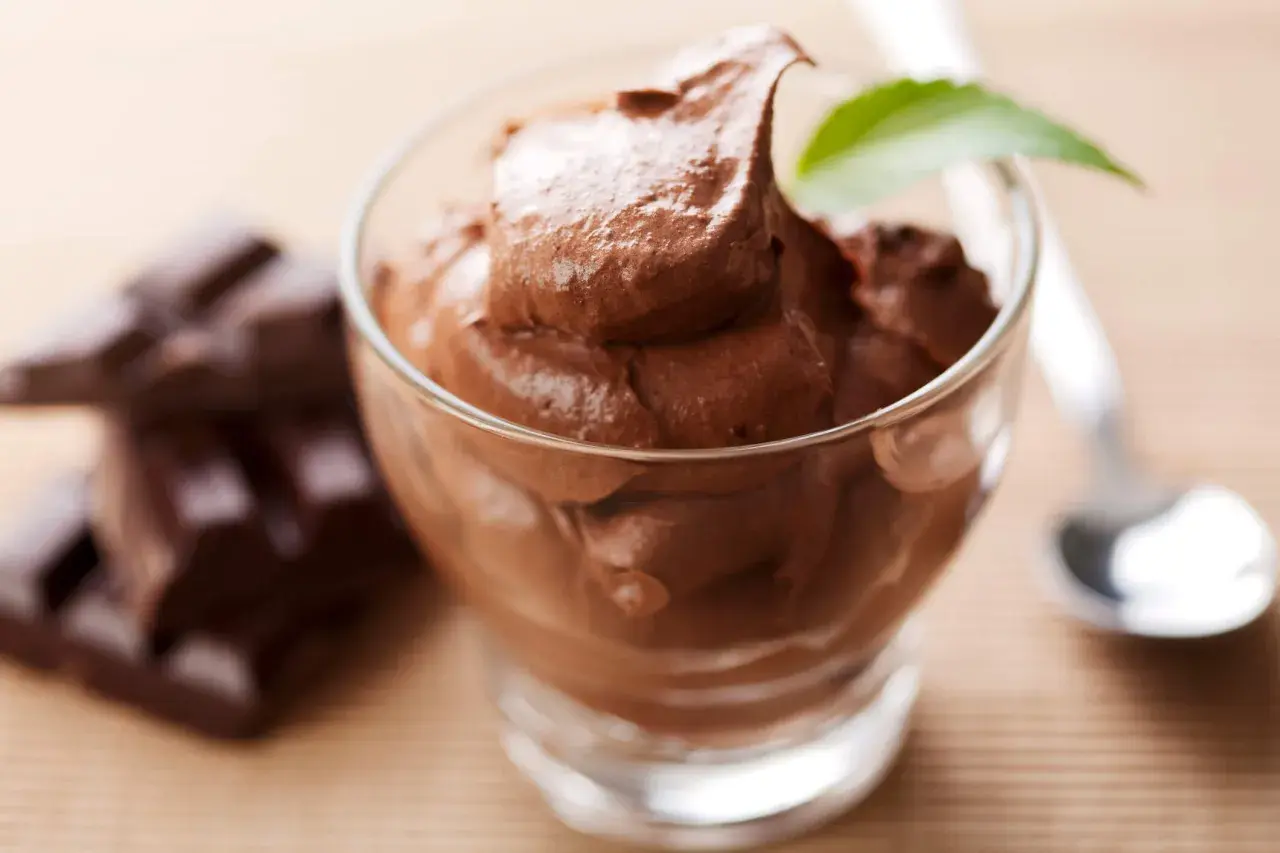 Chokladig kaseinpudding i ett glas, med chokladbitar och en sked i bakgrunden.