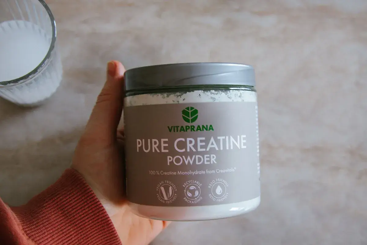 En hand håller en burk med Vitaprana Pure Creatine Powder. Kan vara ett komplement för den som vill ha hjälp med kreatin viktnedgång.