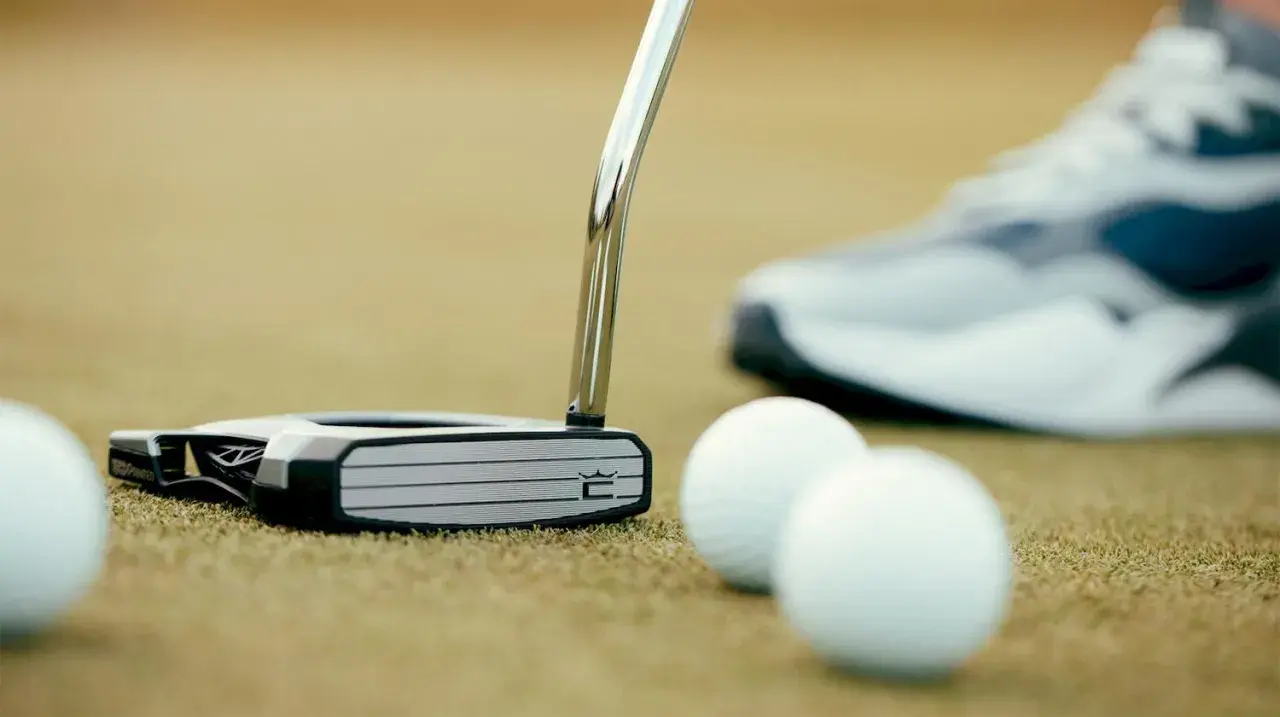 En golfare funderar vilken putter ska man ha. En modern putter ligger på greenen bredvid golfbollar, med en sko i bakgrunden.