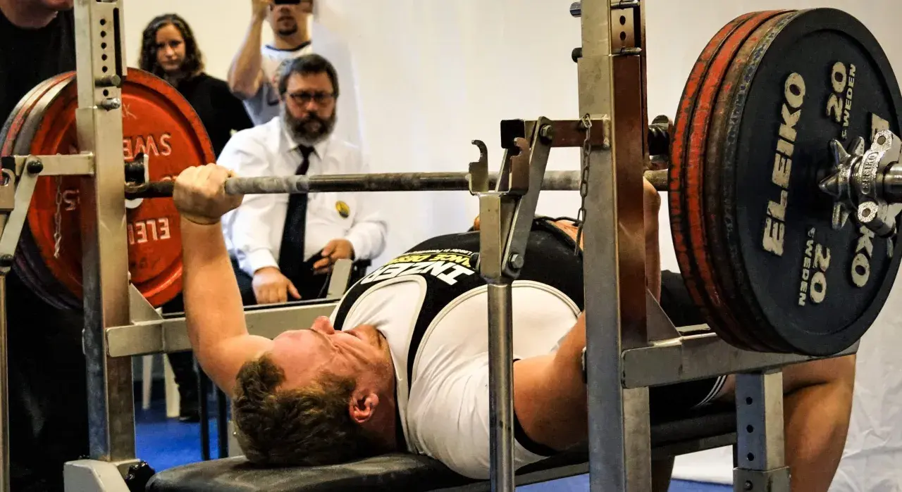 Man utför en floor press med tung vikt på stången. Domare ser på.