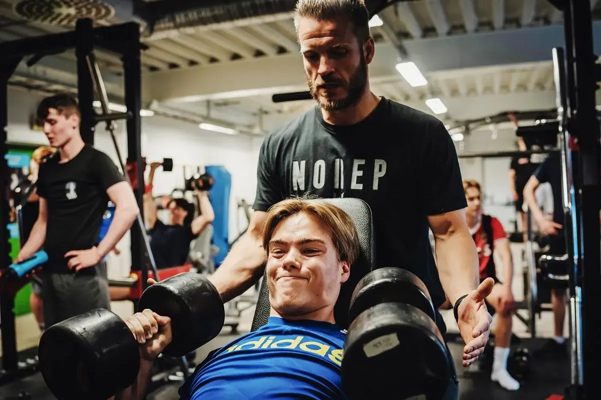Tränare hjälper en ung man med hantlar, en riktig craze pwo-känsla i gymmet.
