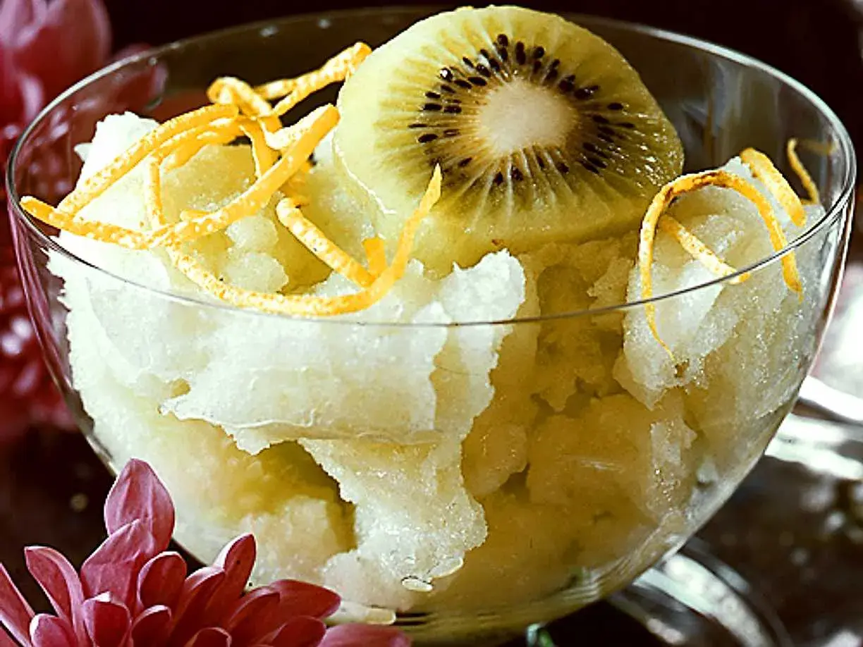 En skål med ljusgul sorbet, toppad med en skiva kiwi och strimlad apelsinskal. En svalkande vattenmelon sorbet för en varm dag.