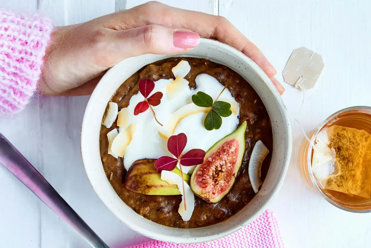 En skål med gröt, yoghurt, fikon och kokosflingor. En perfekt frukost med lite kalorier, serverad med en kopp te.