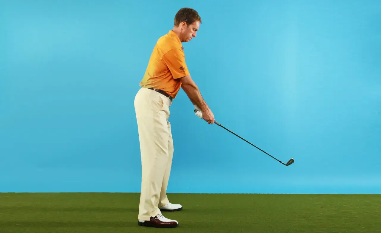 Man i orange pikétröja och beige byxor förbereder sig för ett golfslag. Hans svinghastighet kan påverkas av ålder.