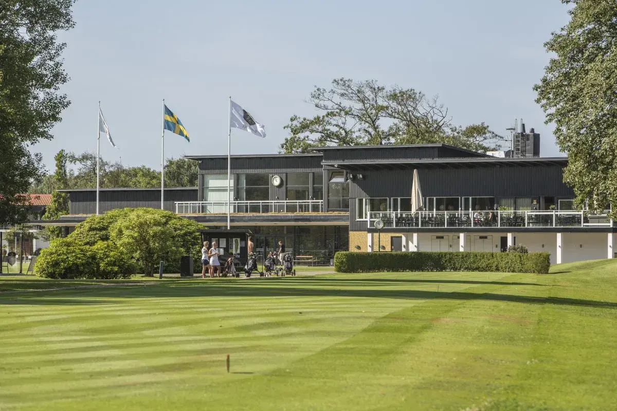 En golfklubb i Sverige med en modern byggnad, flaggor och välklippta fairways. Här kan man höra många golftermer.