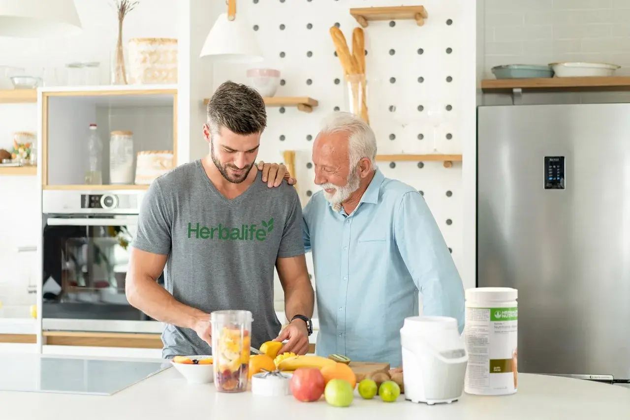 Två män i ett kök förbereder en smoothie. En burk med proteinpulver står på bänken, perfekt för att få rätt mängd protein per dag.