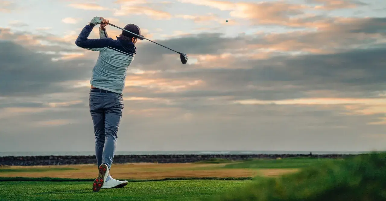 En golfare svingar klubban vid solnedgången. Ett perfekt sätt att använda sitt friskvårdsbidrag för golf.