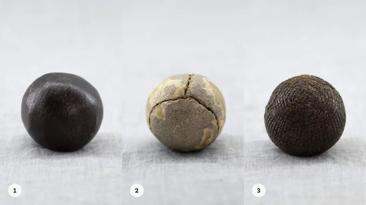 Tre gamla bollar: en mörk, en sprickig och en med rutmönster. Kanske en tidig guttaperka boll?