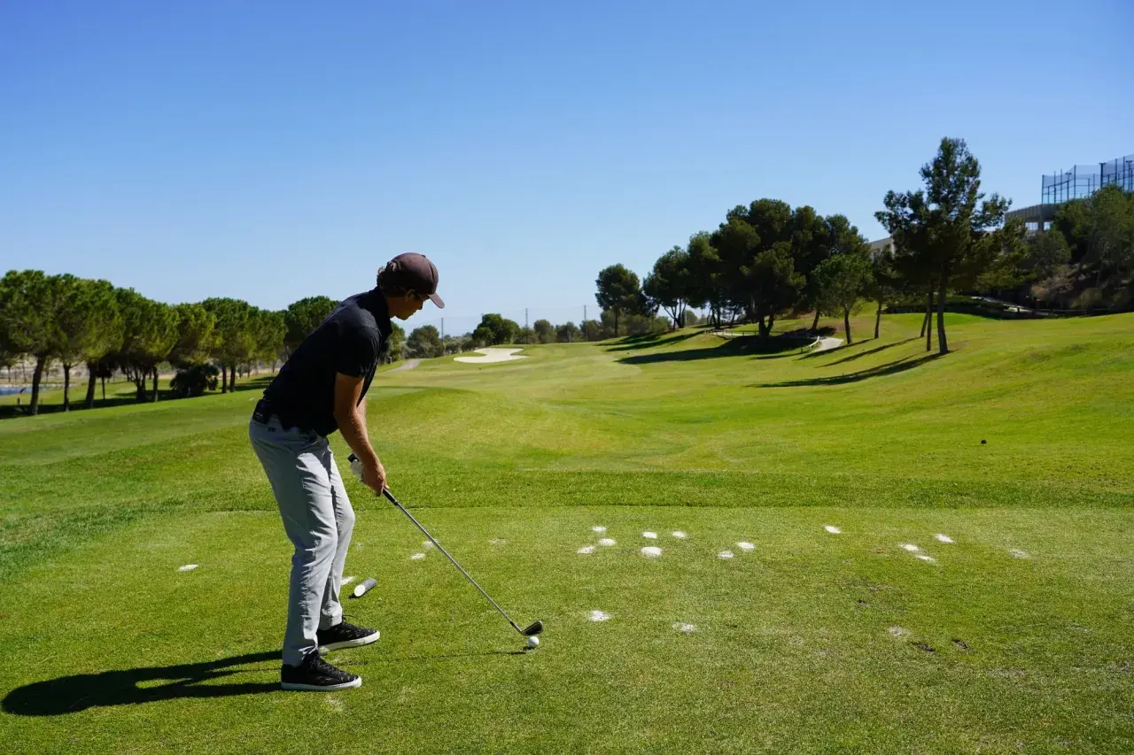 En man förbereder sig för ett slag på en golfbana. Han är klädd i en keps och tröja, redo för olika spelformer golf.