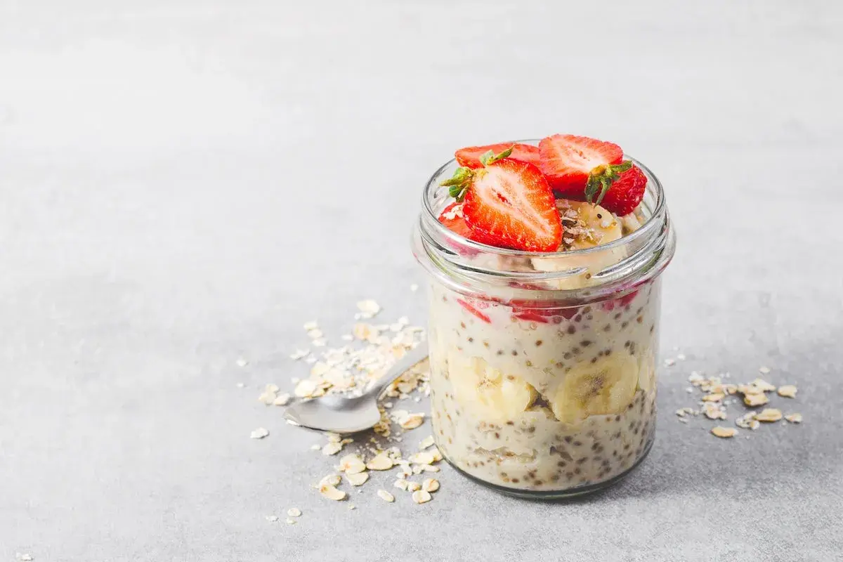 En burk med overnight oats recept toppad med jordgubbar och banan. En sked ligger bredvid med havregryn.