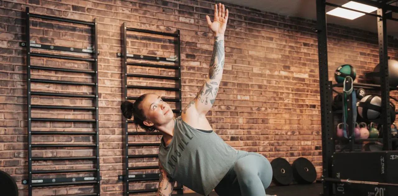Kvinna med tatueringar utför en övning på sitt gymprogram. Hon ligger på sidan med en arm uppsträckt.