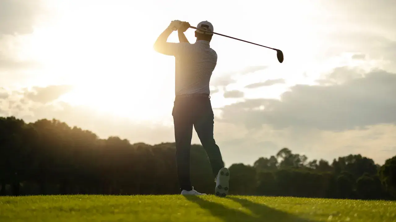 En golfare svingar klubban i solnedgången. Perfekt för en golf flyer.