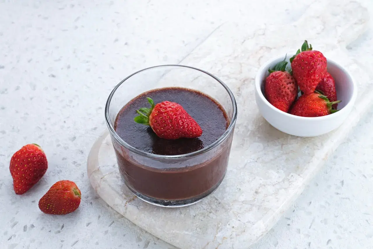 Chokladig proteinpudding i glas, toppad med jordgubbe. Bredvid en skål med färska jordgubbar. Ett enkelt recept på proteinpudding.