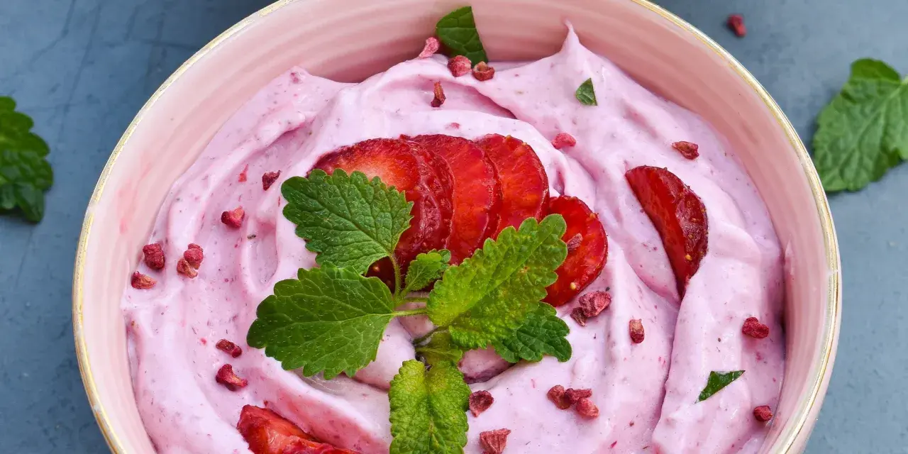 Keso glass med jordgubbar och mynta. En rosa, krämig dessert med färska jordgubbskivor och torkade bär.