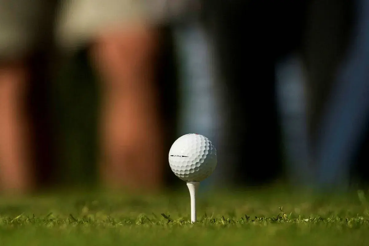 En golfboll i huvudet, redo för ett slag. Gräset är grönt och bakgrunden suddig.