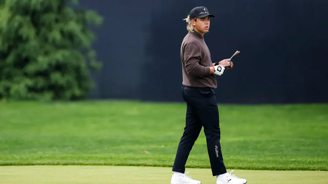Golfare i brun tröja och keps går på banan, funderar på vad betyder vit markering på banan?