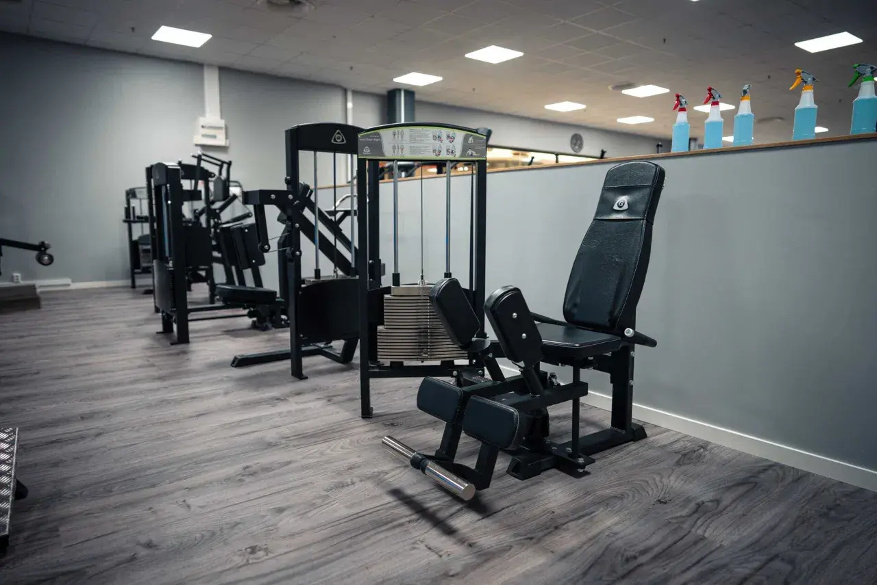 En adduktormaskin i ett modernt gym. Maskinen är svart med vadderade dynor och en viktstapel.