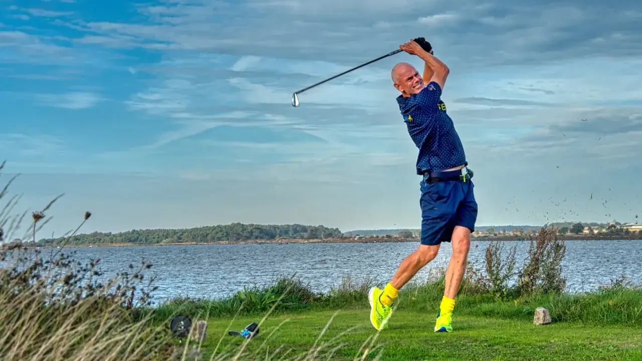 Man i full sving på golfbanan, redo för en perfekt drive. Vacker utsikt över vattnet.