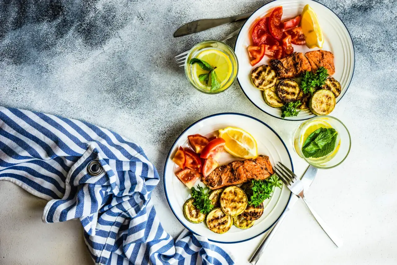 Två tallrikar med grillad lax, tomatklyftor och grillad zucchini. Perfekt för en måltid med inga kolhydrater.