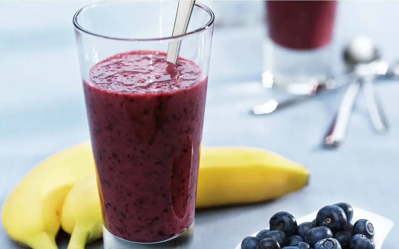 En glas med proteinrik smoothie, bananer och blåbär. Perfekt för en energifylld start på dagen.