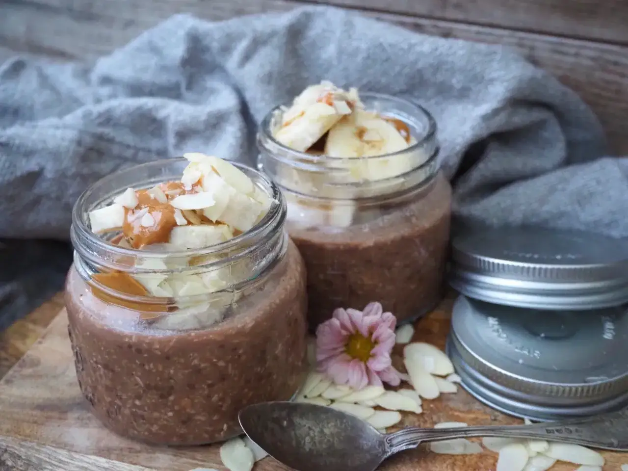 Två burkar med overnight oats choklad, toppade med banan, mandel och kolasås. En perfekt frukost att förbereda kvällen innan.