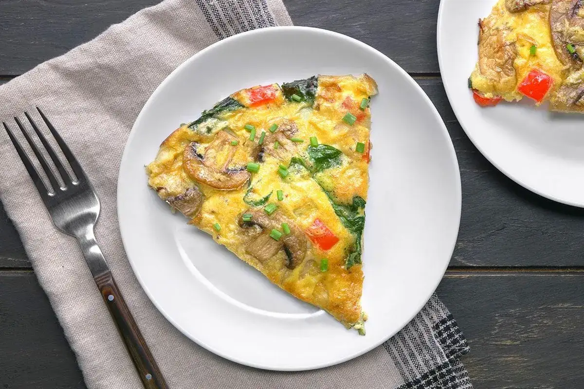En bit frittata med svamp, spenat och paprika på en vit tallrik. En perfekt frukost utan kolhydrater.