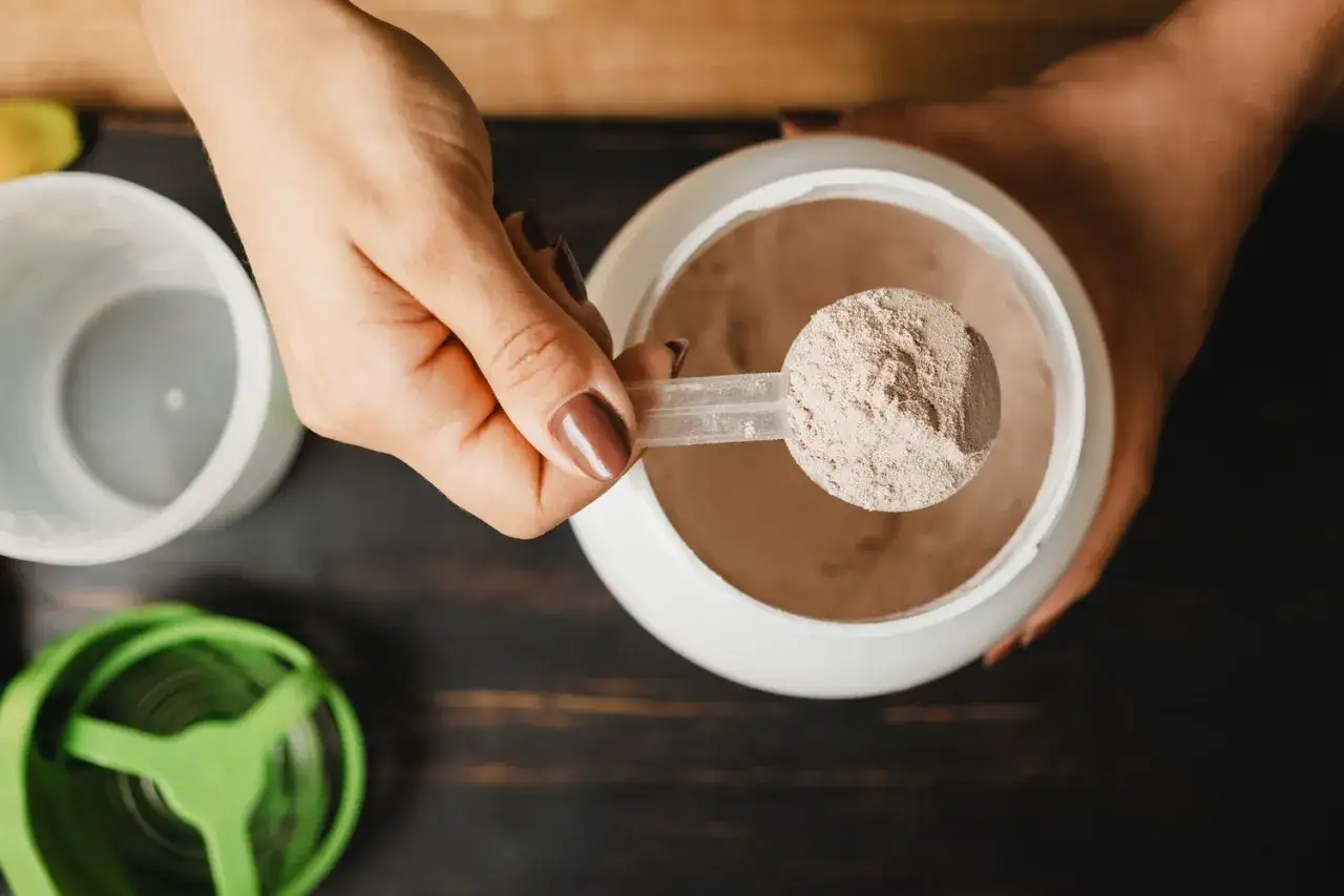 En hand håller en skopa med proteinpulver. Frågan om hur mycket kreatin per dag är relevant för att optimera träningen.