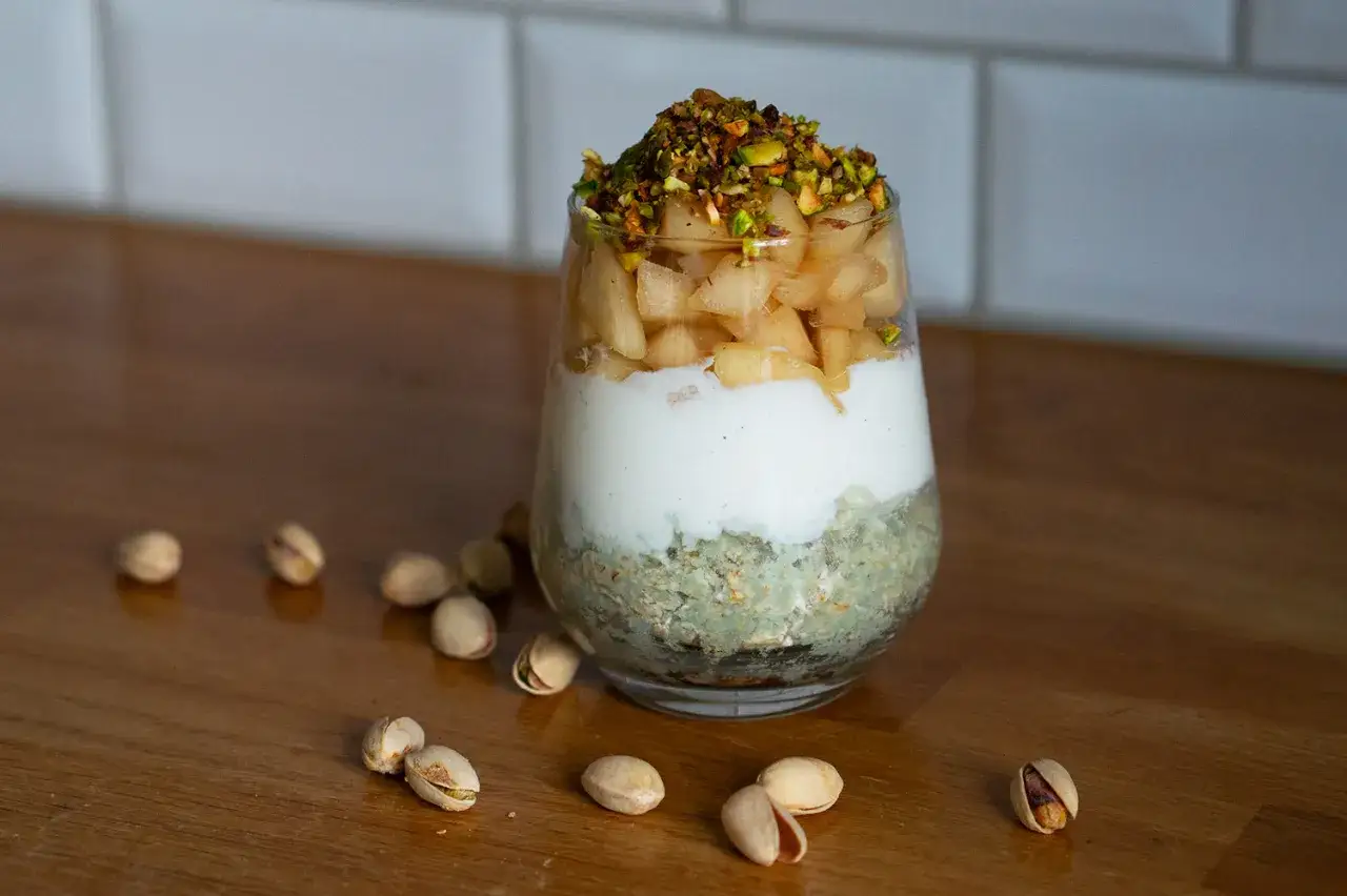 En glasburk med overnight oats saffran, yoghurt, äppelbitar och pistagenötter.