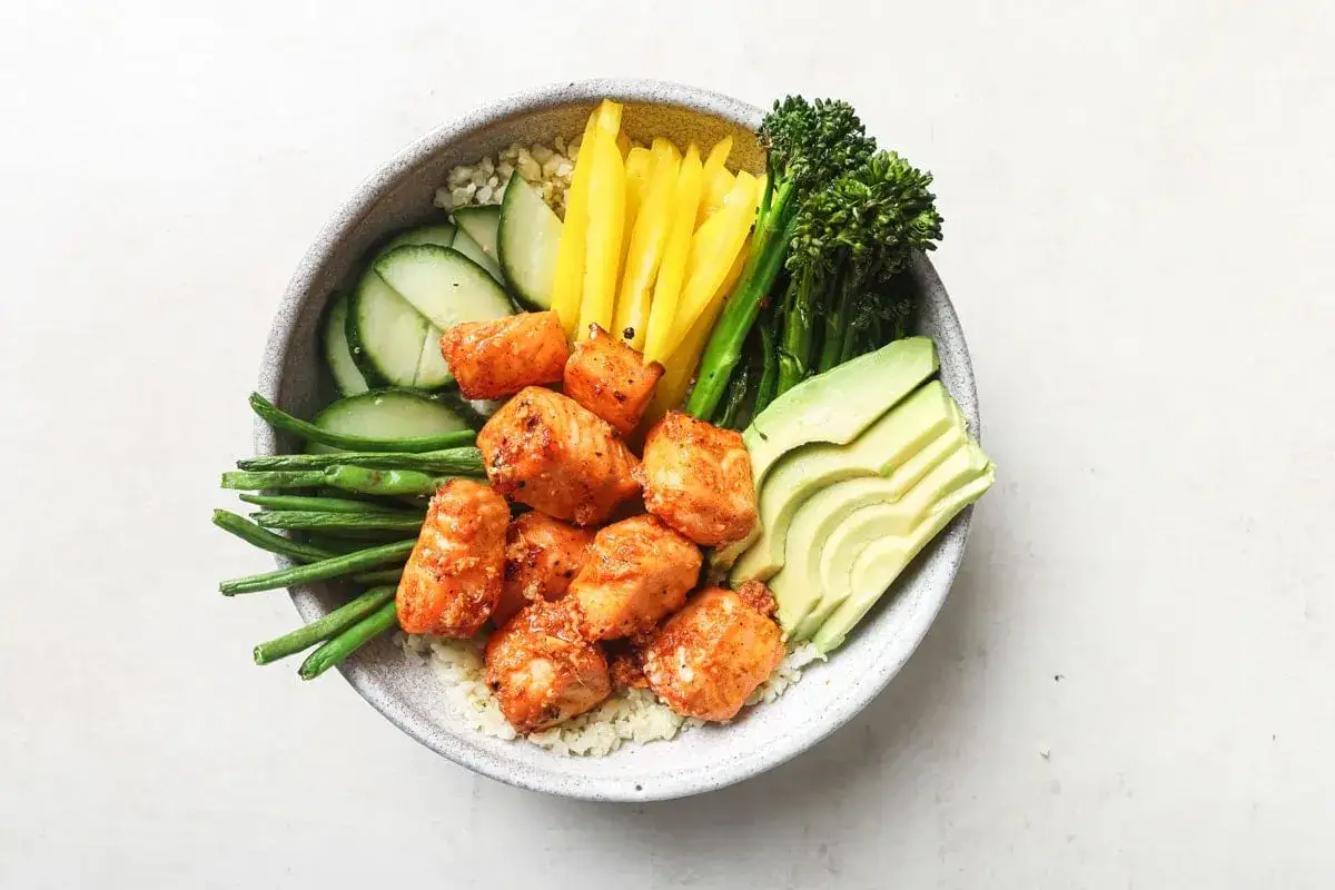 En h&auml;lsosam bowl med laxbitar som ger 30g protein, serverad med ris, gurka, haricots verts, paprika, broccoli och avokado.