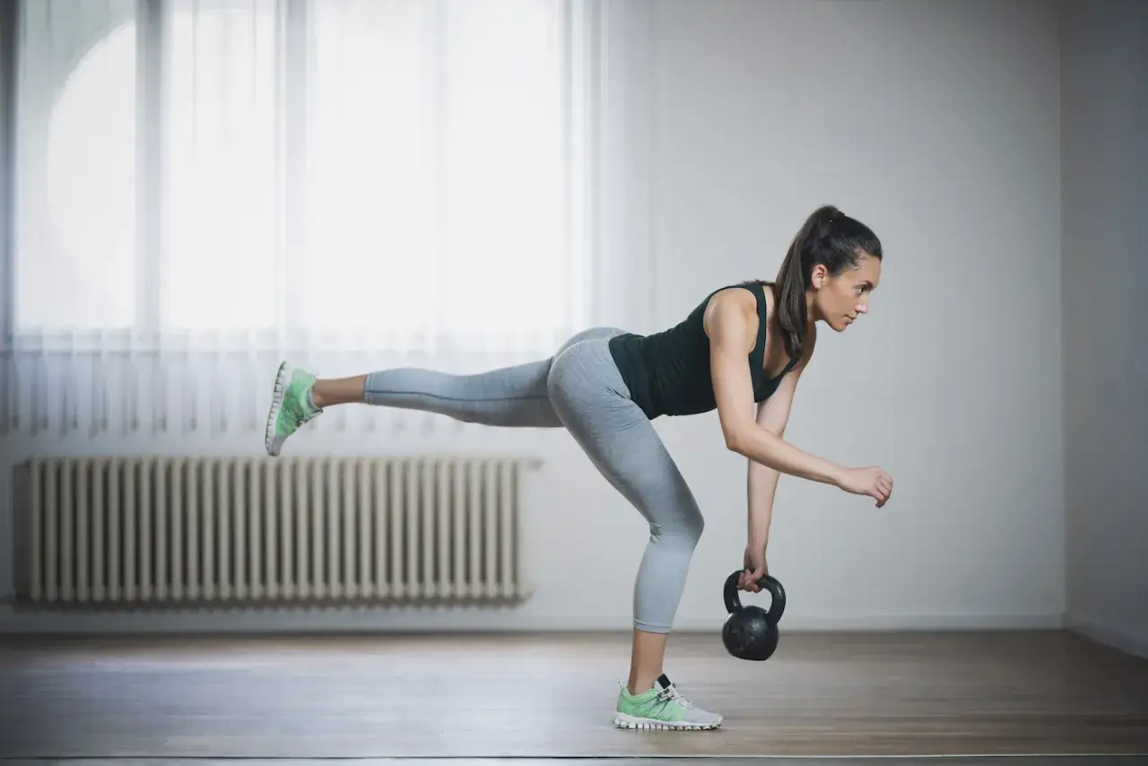 Kvinna utför enbens marklyft med kettlebell. Hon balanserar på ett ben med det andra rakt bakåt.