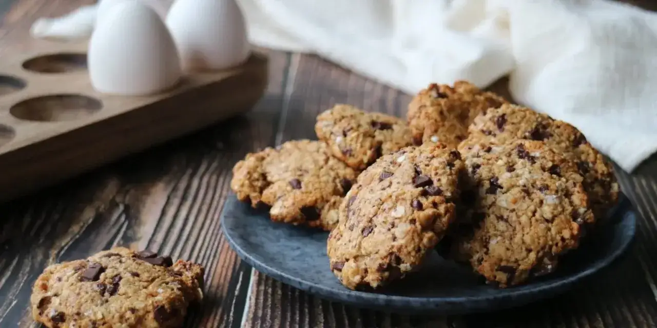 Chokladkakor med havregryn och nötter, perfekta för ett enkelt proteinkakor recept. Ägg i bakgrunden antyder att bakningen är på gång.