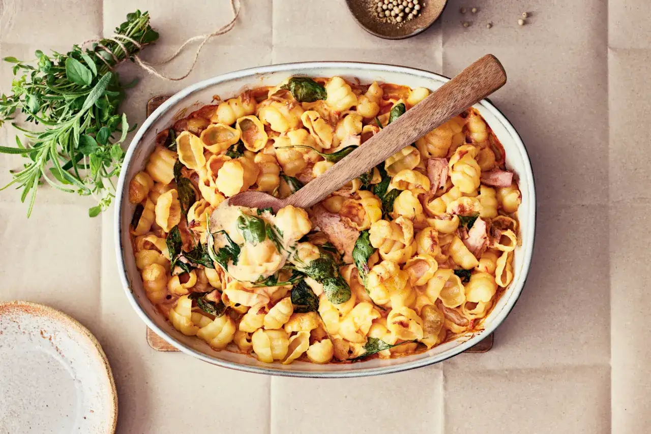 En krämig pastarätt med skruvpasta, spenat och skinka. Ett perfekt recept med ingredienser man har hemma, serverad i en ugnsform med en träsked.