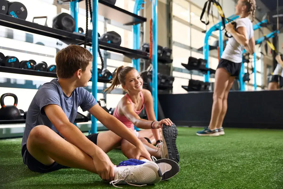 Två ungdomar stretchar på ett gym, en tredje tränar i bakgrunden.