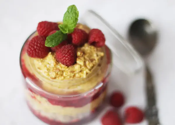 En burk med overnight oats med saffranssmak, toppad med hallon och mynta. En sked ligger bredvid.